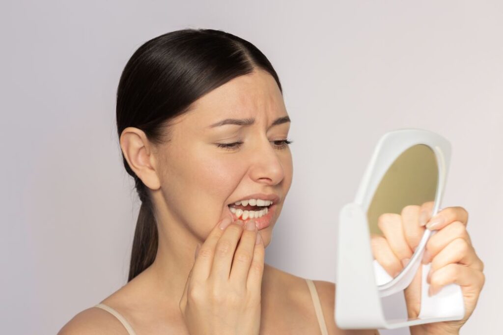 A woman examining her gums in a mirror.