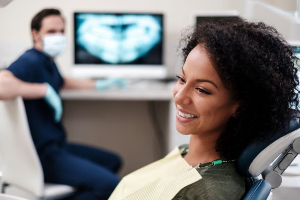 A woman sitting in a dentist’s chair with a dentist in the background